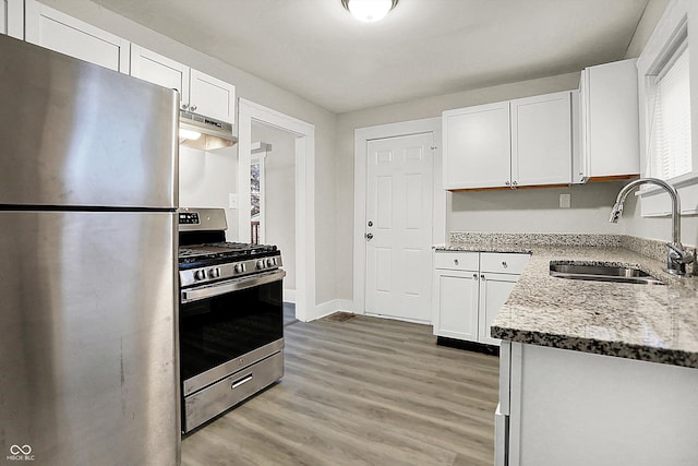 kitchen with sink, white cabinetry, light stone counters, appliances with stainless steel finishes, and hardwood / wood-style flooring