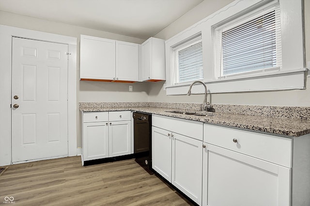 kitchen featuring black dishwasher, sink, light stone countertops, and white cabinets