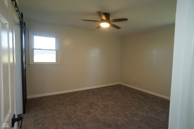 unfurnished room with a barn door, ceiling fan, crown molding, and dark carpet