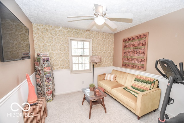 living area with a ceiling fan, wainscoting, a textured ceiling, and carpet flooring