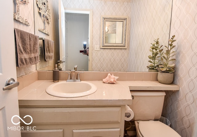 half bath featuring toilet, wallpapered walls, and vanity