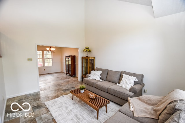 living area with stone finish floor, a notable chandelier, a towering ceiling, and baseboards