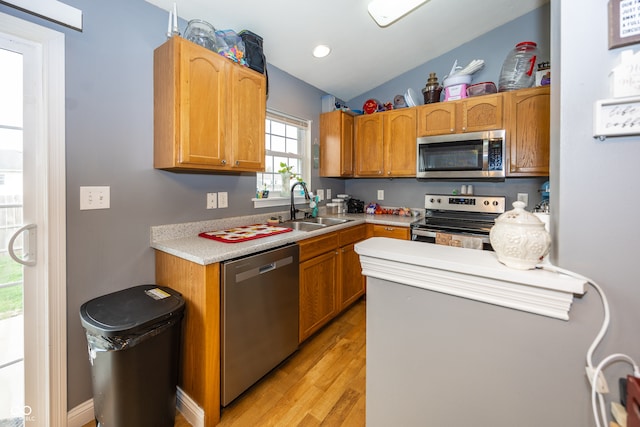 kitchen with light wood-type flooring, stainless steel appliances, vaulted ceiling, and sink