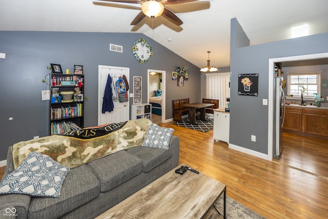 living room featuring ceiling fan with notable chandelier, vaulted ceiling, light hardwood / wood-style flooring, and sink