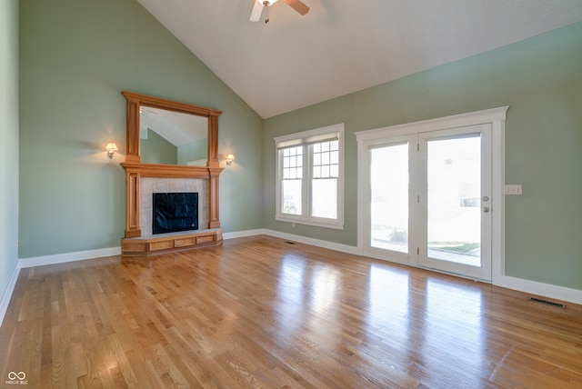 unfurnished living room with ceiling fan, a tile fireplace, light wood-type flooring, and high vaulted ceiling