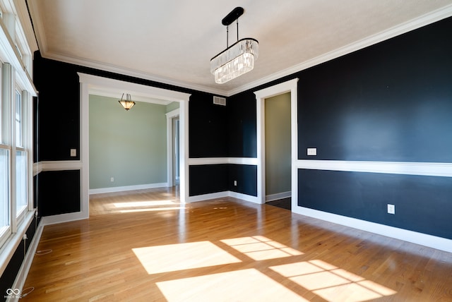 spare room featuring ornamental molding, light wood-type flooring, and a chandelier