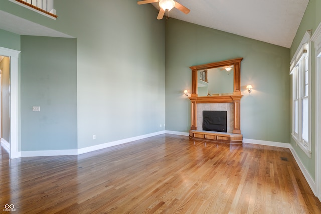 unfurnished living room featuring hardwood / wood-style floors, ceiling fan, high vaulted ceiling, and a tile fireplace