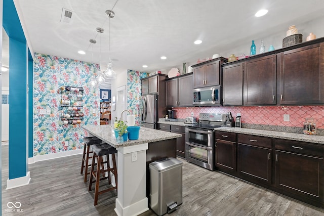 kitchen with hanging light fixtures, light stone countertops, an island with sink, light hardwood / wood-style floors, and stainless steel appliances