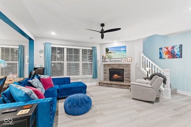 living room featuring light hardwood / wood-style flooring, ceiling fan, and a stone fireplace