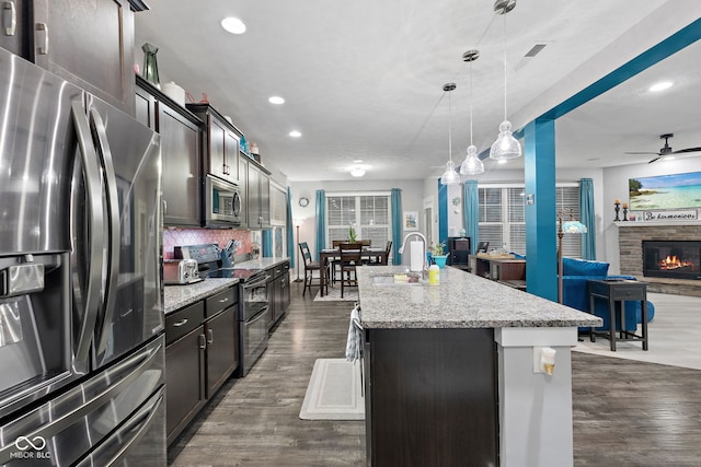 kitchen featuring hanging light fixtures, decorative backsplash, an island with sink, appliances with stainless steel finishes, and dark hardwood / wood-style flooring