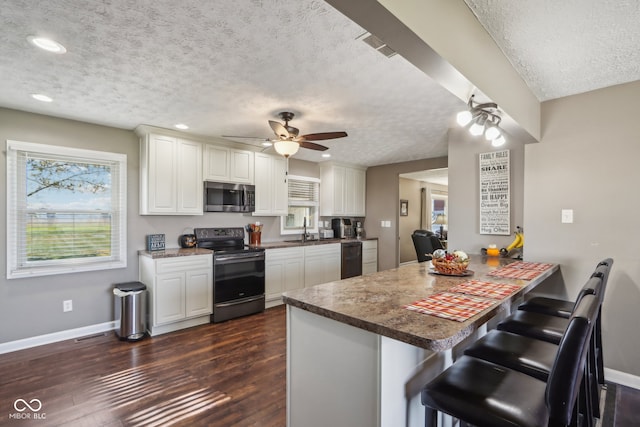 kitchen featuring black appliances, dark hardwood / wood-style floors, a breakfast bar, white cabinets, and kitchen peninsula