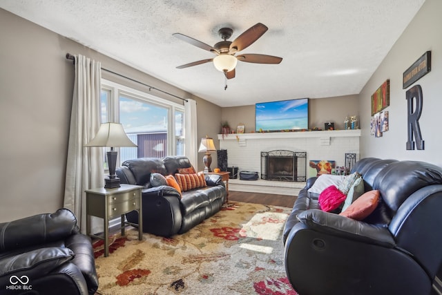 living room featuring a textured ceiling, wood-type flooring, ceiling fan, and a fireplace