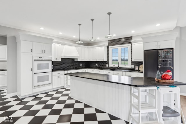 kitchen featuring custom exhaust hood, black fridge with ice dispenser, white double oven, a center island, and white cabinetry