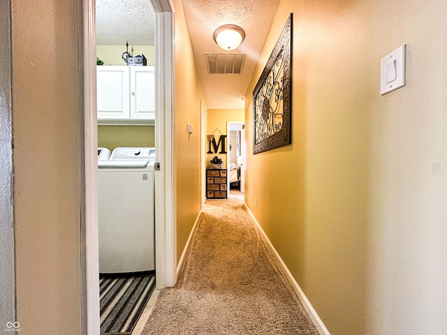 hall featuring a textured ceiling, washing machine and dryer, carpet flooring, visible vents, and baseboards