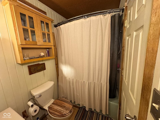 bathroom featuring wooden walls, toilet, a textured ceiling, and shower / bathtub combination with curtain