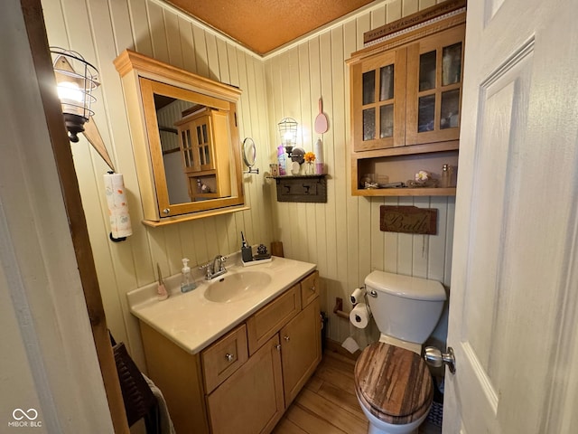 bathroom featuring vanity, wood walls, a textured ceiling, and toilet