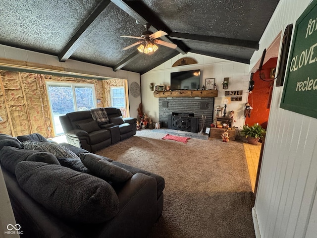 living room featuring ceiling fan, a textured ceiling, carpet, a fireplace, and lofted ceiling with beams