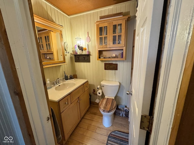 bathroom with wood-type flooring, vanity, a textured ceiling, wooden walls, and toilet