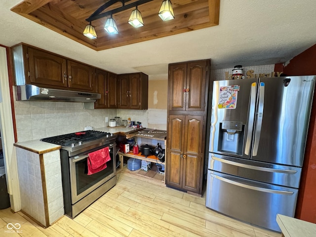 kitchen featuring tasteful backsplash, stainless steel appliances, dark brown cabinets, pendant lighting, and light hardwood / wood-style flooring