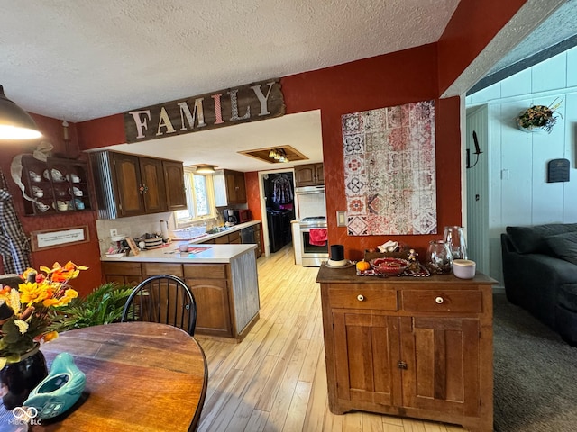 kitchen with light hardwood / wood-style floors, a textured ceiling, kitchen peninsula, and stainless steel range oven