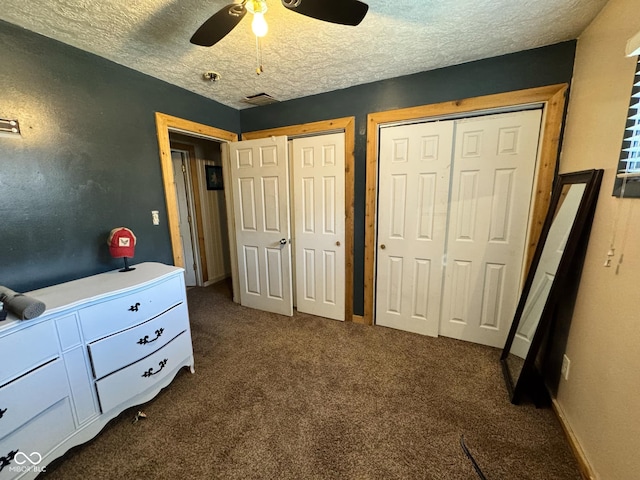 bedroom with ceiling fan, a textured ceiling, two closets, and dark carpet