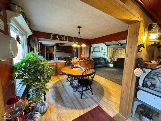 dining area featuring wood walls, a textured ceiling, and light wood-type flooring