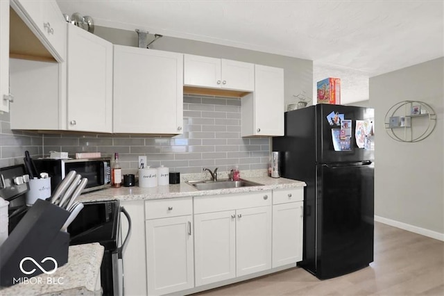 kitchen with black refrigerator, sink, and white cabinets