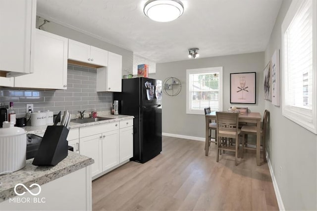 kitchen with black refrigerator, sink, tasteful backsplash, white cabinetry, and light hardwood / wood-style flooring