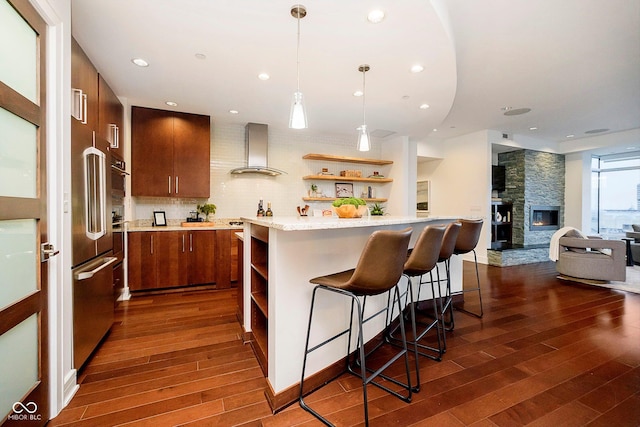 kitchen with a center island, wall chimney exhaust hood, dark wood-type flooring, backsplash, and a fireplace