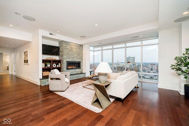 living room with a healthy amount of sunlight, a stone fireplace, a wall of windows, and dark wood-type flooring