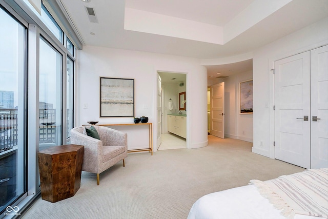 bedroom featuring ensuite bathroom, a closet, light colored carpet, and a tray ceiling