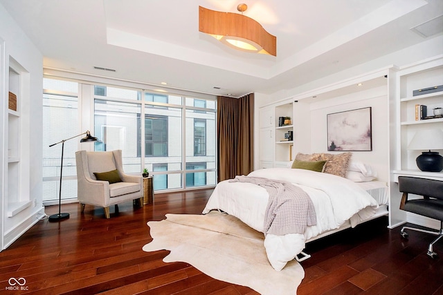 bedroom featuring dark hardwood / wood-style floors, a raised ceiling, and a wall of windows