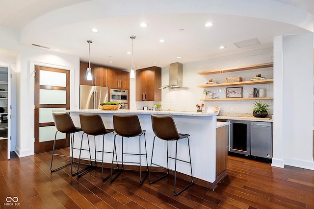 kitchen with a kitchen bar, decorative backsplash, wall chimney exhaust hood, stainless steel appliances, and decorative light fixtures