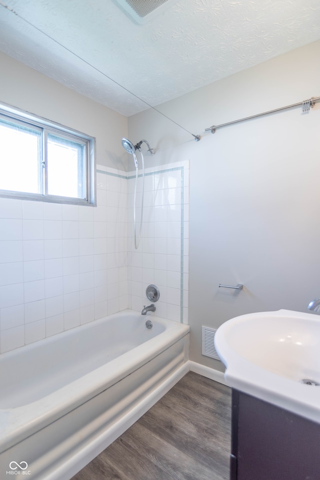 bathroom with hardwood / wood-style flooring, a textured ceiling, and tiled shower / bath