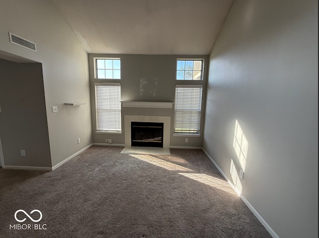 unfurnished living room with carpet flooring, a high ceiling, and a tiled fireplace