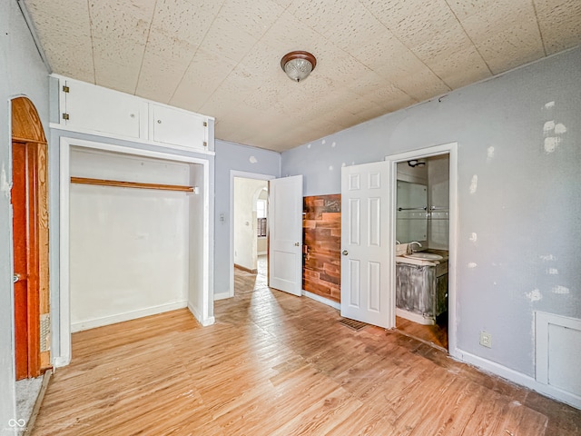 unfurnished bedroom with connected bathroom, a closet, light wood-type flooring, and sink