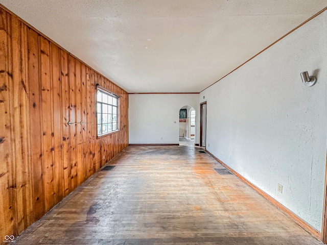 unfurnished room featuring wood walls, hardwood / wood-style flooring, and crown molding