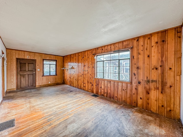 spare room featuring light hardwood / wood-style floors, wooden walls, and a textured ceiling