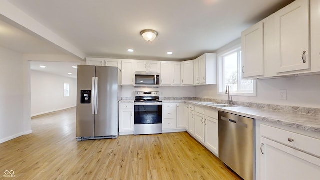 kitchen with stainless steel appliances, white cabinets, sink, and light hardwood / wood-style flooring