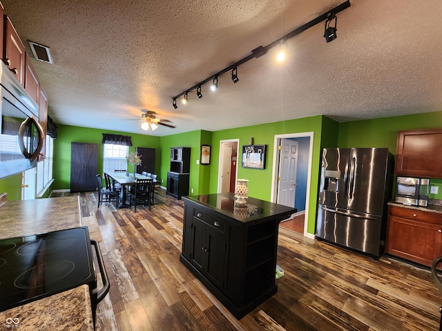 kitchen with appliances with stainless steel finishes, a textured ceiling, dark hardwood / wood-style floors, and a center island