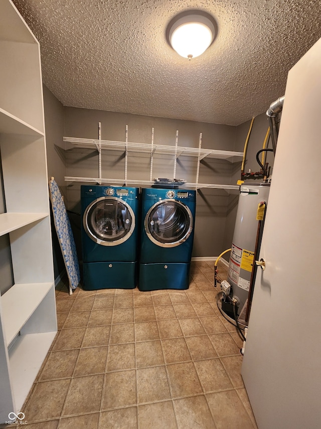 laundry area featuring water heater, washing machine and dryer, a textured ceiling, and light tile patterned flooring