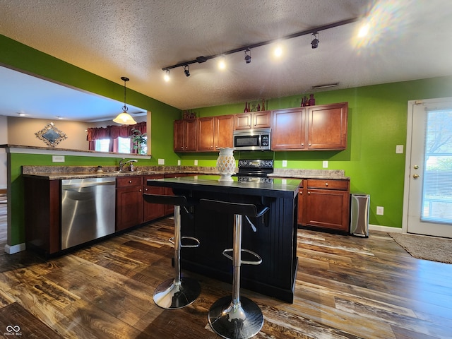 kitchen with dark wood-type flooring, appliances with stainless steel finishes, decorative light fixtures, and a breakfast bar area