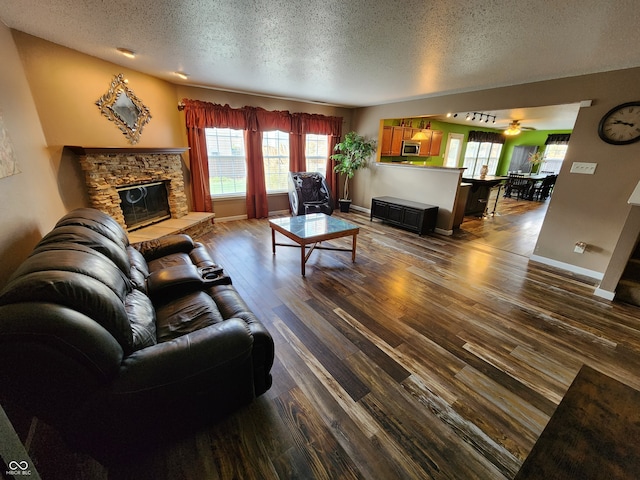 living room featuring a stone fireplace, hardwood / wood-style floors, a textured ceiling, and ceiling fan