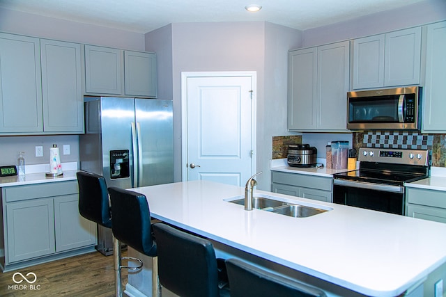 kitchen with dark wood-type flooring, a center island with sink, sink, gray cabinets, and stainless steel appliances