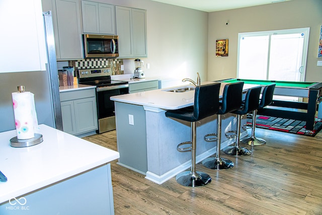 kitchen with appliances with stainless steel finishes, light hardwood / wood-style floors, a kitchen island with sink, and gray cabinetry