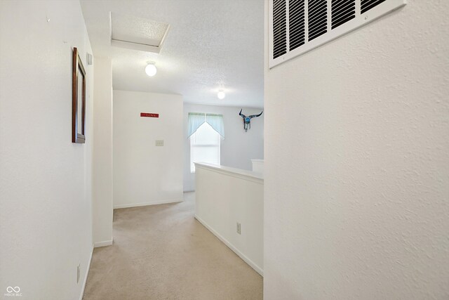 hallway with a textured ceiling and light colored carpet