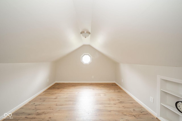 additional living space featuring lofted ceiling, light hardwood / wood-style flooring, and built in shelves