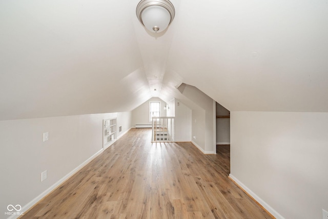 additional living space with built in shelves, vaulted ceiling, light hardwood / wood-style flooring, and a baseboard heating unit