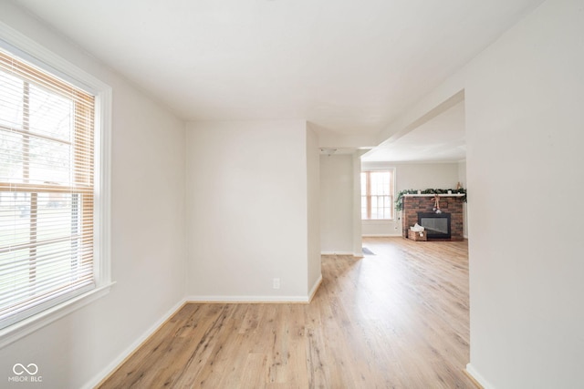 spare room with a brick fireplace and light wood-type flooring