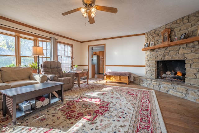 living room with crown molding, a stone fireplace, a textured ceiling, hardwood / wood-style floors, and ceiling fan